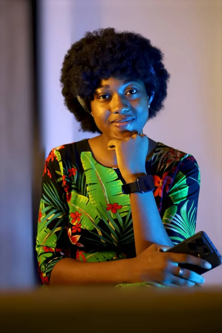 Ekene Ngwudike, smiling, chin resting on her hand, in a green tropical-print top